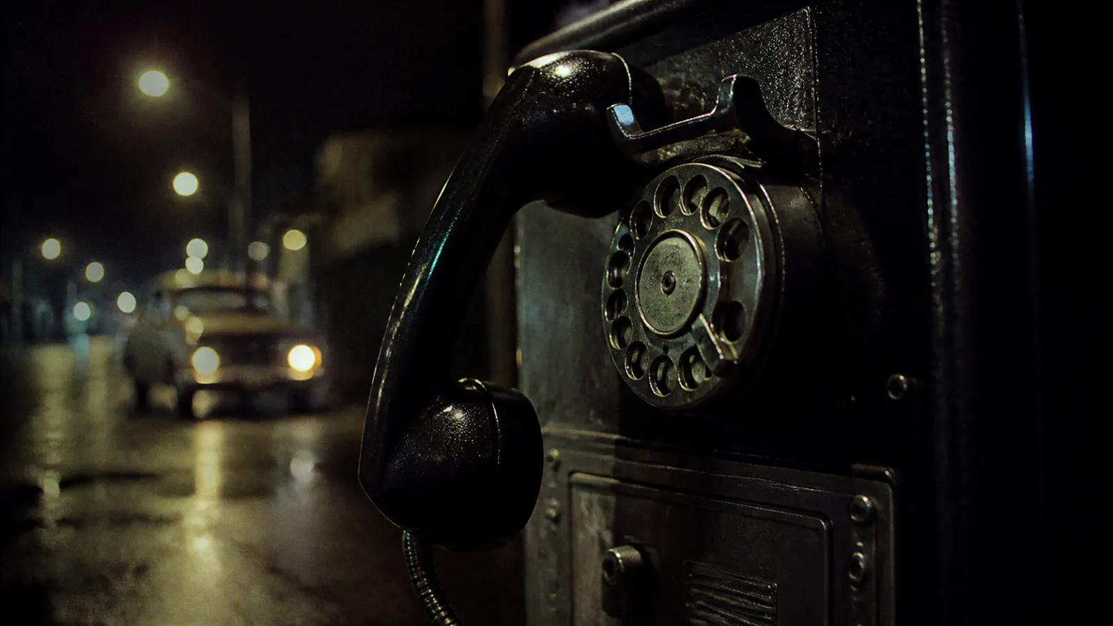 Close-up of a vintage black rotary telephone receiver resting off the hook on a payphone at night
